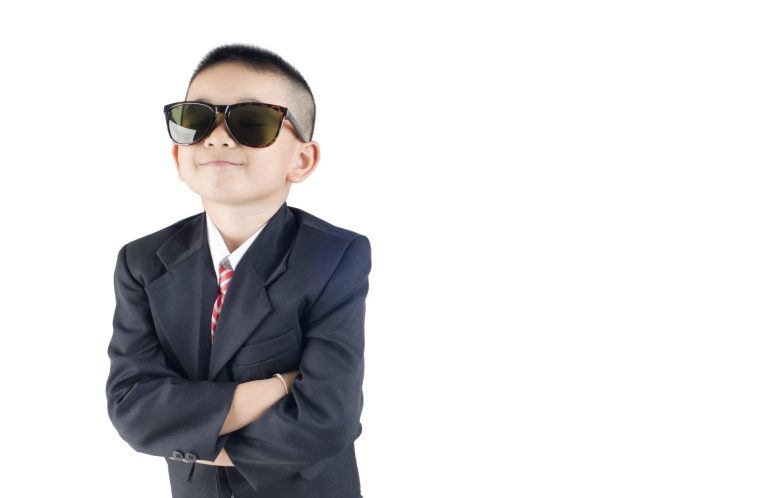 Ein selbstbewusster Junge in einem Anzug und Sonnenbrille, mit verschränkten Armen.