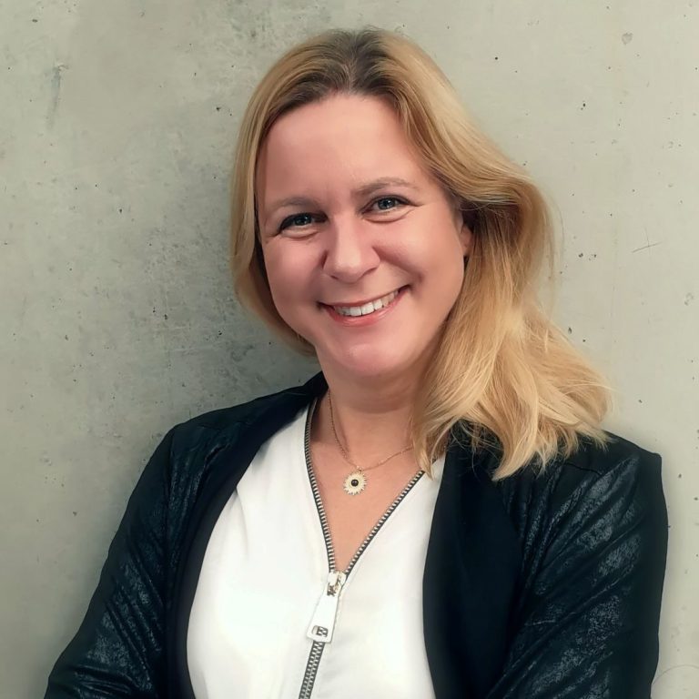 Bild von Kerstin Brenner, lange blonde Haare, schwarze Jacke, sie strahlt in die Kamera 