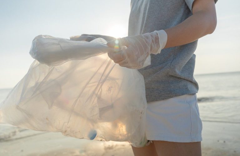 Person mit Handschuhen sammelt Müll am Strand bei Sonnenlicht.