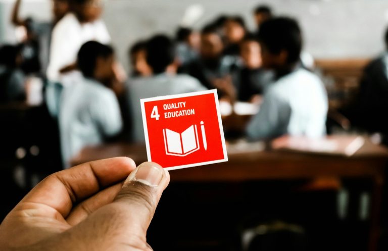 Hand hält ein rotes Symbol mit der Aufschrift "4 Lesen", Schüler im Hintergrund.