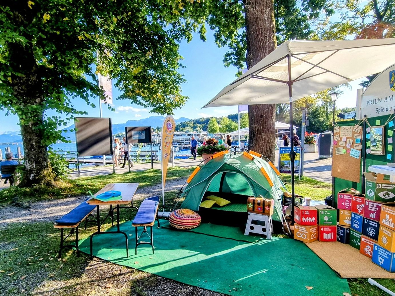 Diverse Menschen unter einem Regenbogen und der Erdkugel mit 3 abklatschenden Personen in der Mitte und den 17 Nachhaltigkeitszielen SDGs. 